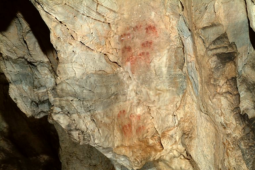 Abstract ochre marks and hand stencils on limestone walls inside Cueva de Ardales, Málaga — among the oldest cave art in Europe, dating to over 65,000 years ago.